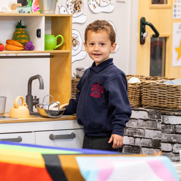 A boy is playing by the pretend kitchen area in the Red House Nursery.